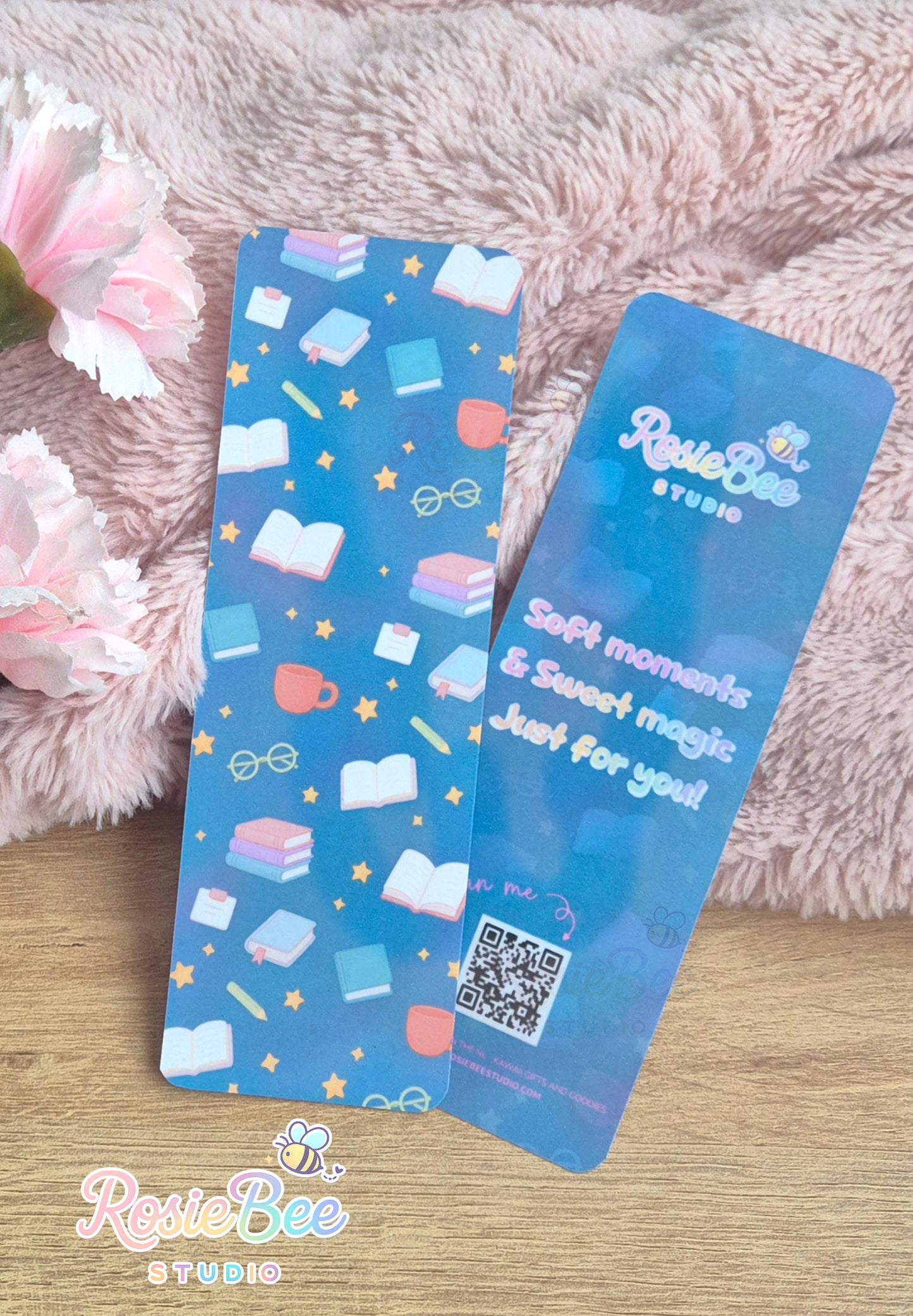 Donkerblauwe boekenlegger met boeken en sterren patroon en quote achterkant, gefotografeerd op zachte roze deken met bloemen.