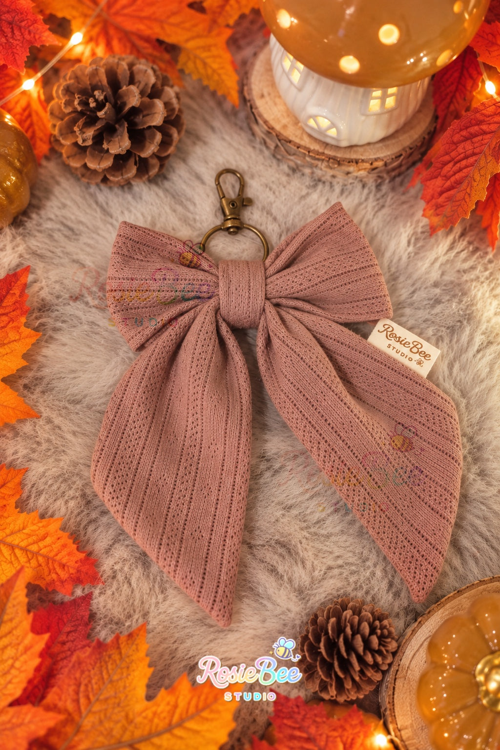 Handgemaakte Autumn Bow sleutelhanger van RosieBee Studio in oudroze stof met opengewerkt patroon en bronskleurige metalen sluiting.