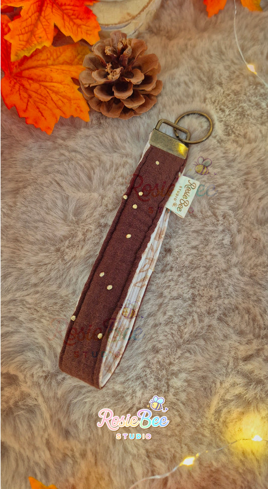 Handgemaakte Golden Pages wristlet van RosieBee Studio met donkerbruine hydrofiel met gouden stipjes, botanische rib jersey en bronskleurige hardware.