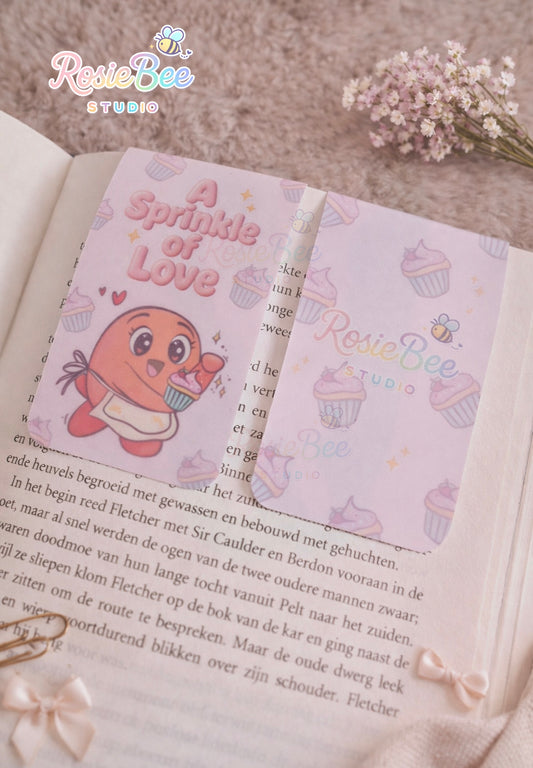 Magnetische boekenlegger “A Sprinkle of Love” met Moji Friend Liefde op een open boek in cosy setting met bloemen en strikjes.