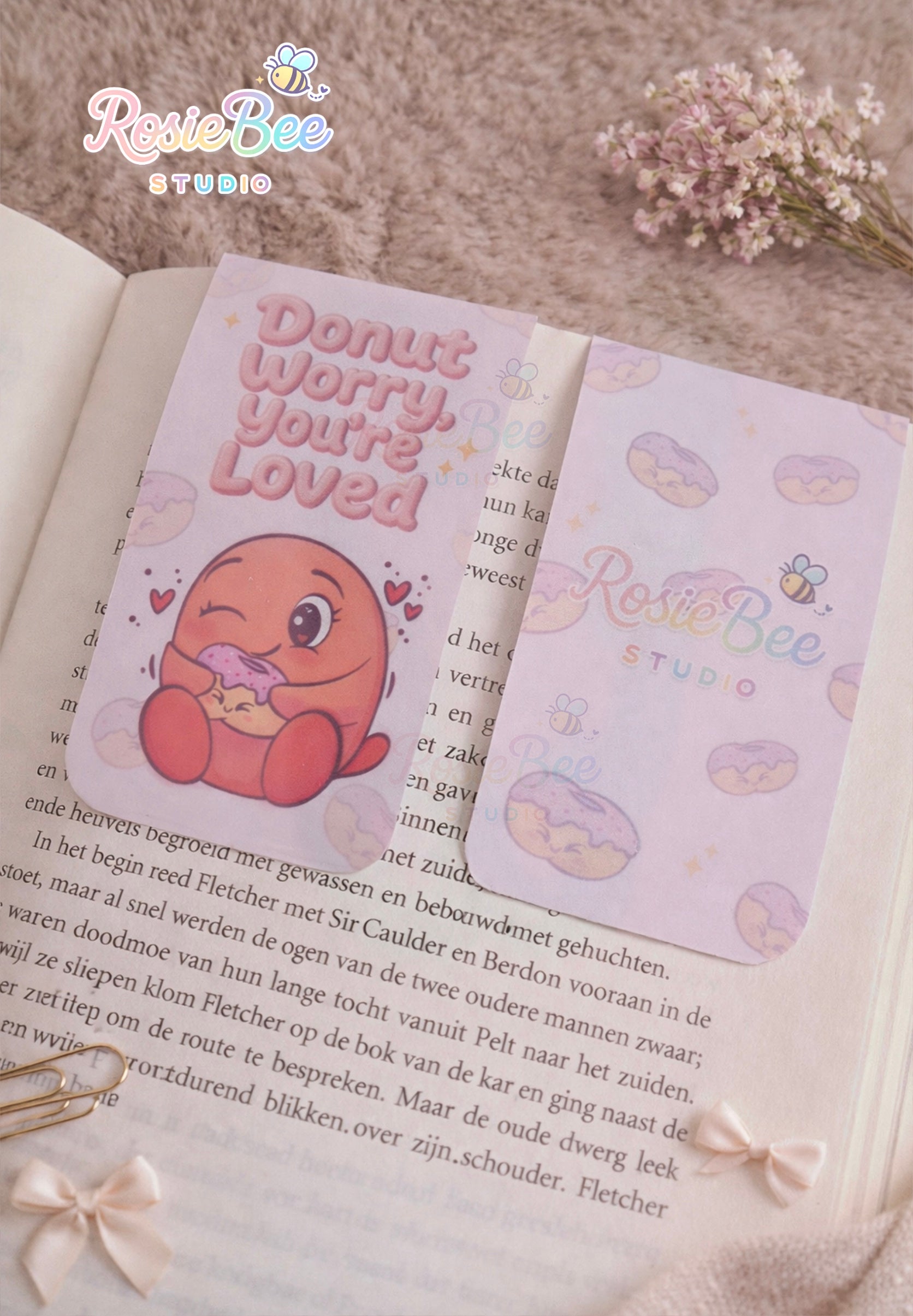 Magnetische boekenlegger “Donut Worry, You’re Loved” met Moji Friend Liefde op een open boek in cosy setting met strikjes en bloemen.