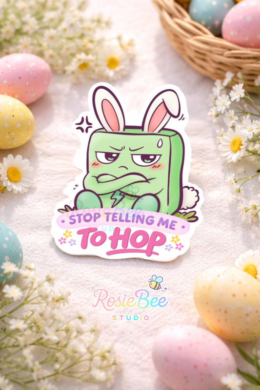 Glossy vinyl sticker van Moji Friend Boosheid met bunny-oortjes en de quote “Stop Telling Me To Hop”, liggend tussen pastel paaseieren en kleine witte bloemetjes.