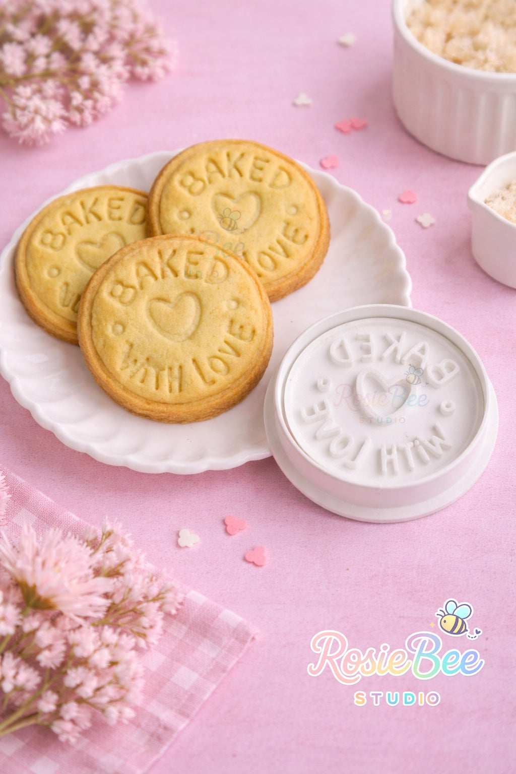 “Baked with love” koekjesstempel (cookie cutter) uit de Moji Friends Cosy Café collectie met ronde koekjes op een wit bordje, pastelroze achtergrond en bloemetjes.