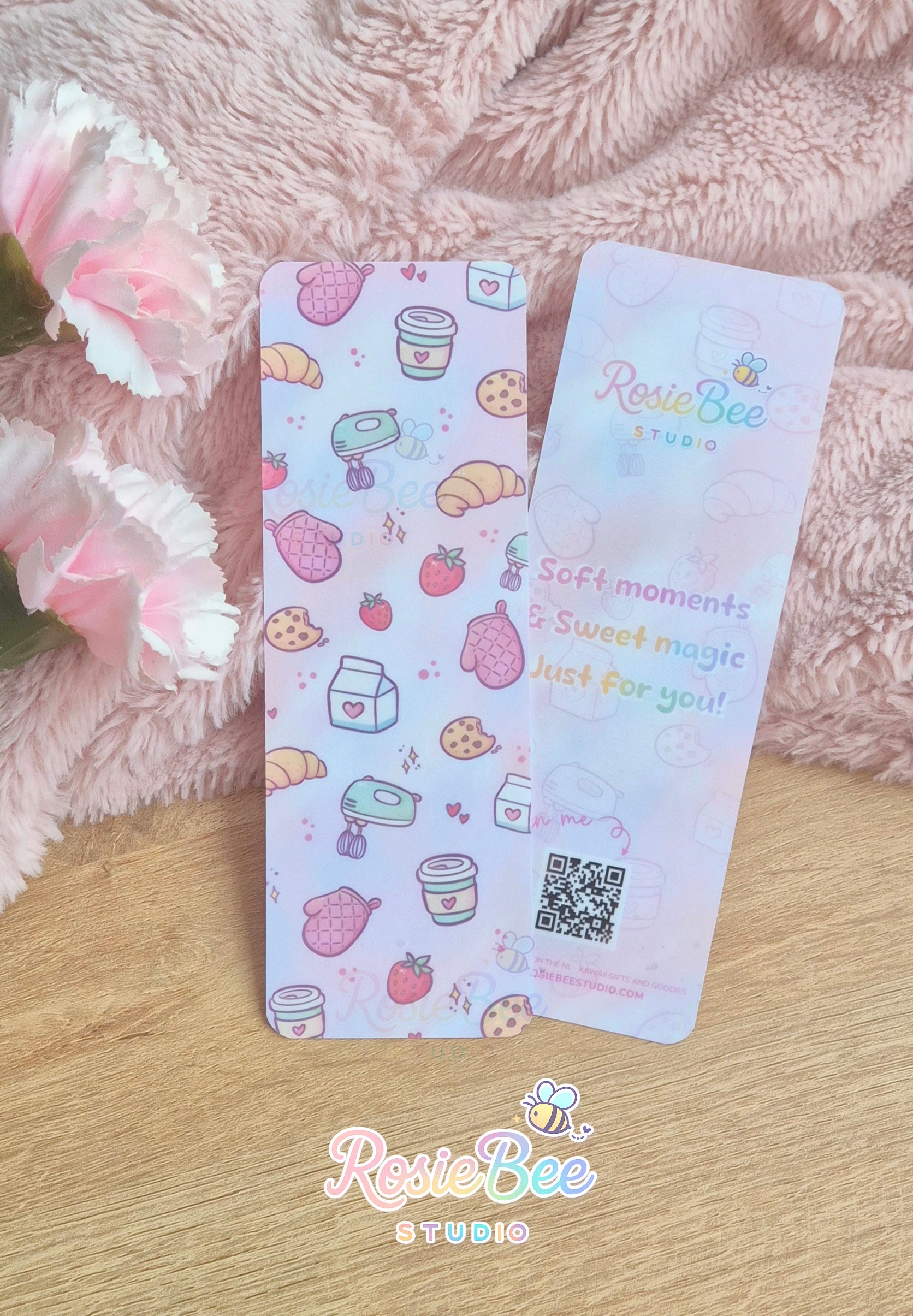 Moji Friends Cosy Café boekenlegger met pastel bakery patroon aan de voorkant en quote aan de achterkant, gefotografeerd op zachte roze deken met bloemen.