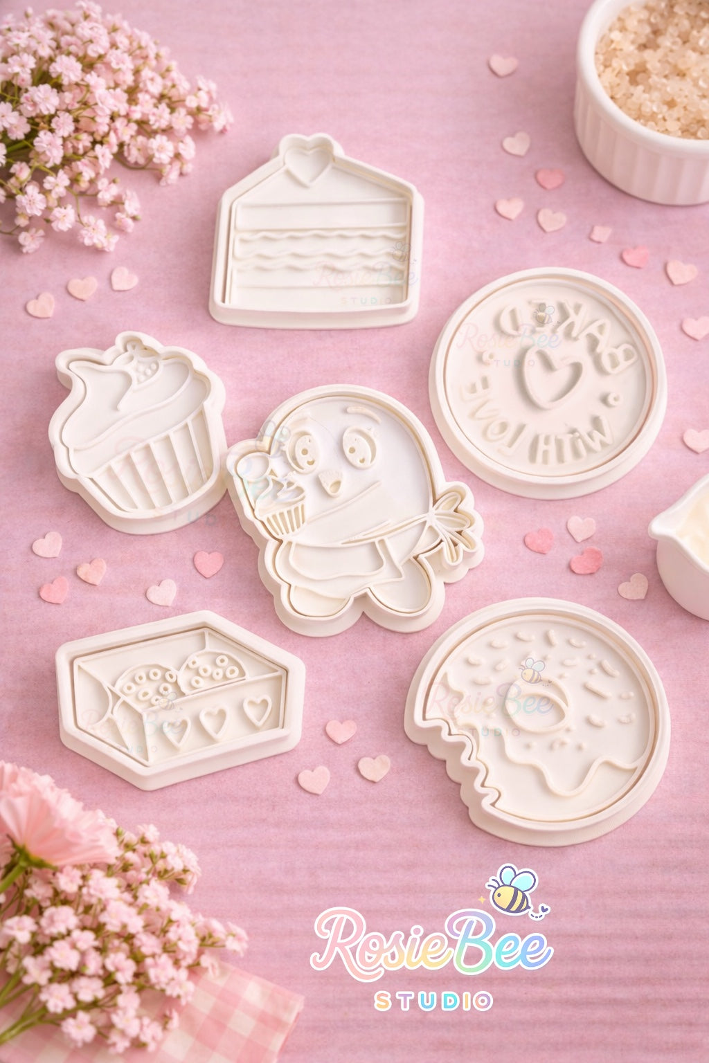 Moji Friends Cosy Café cookie cutter set met 6 koekjesvormpjes op pastelroze achtergrond, inclusief cupcake, donut, gebakje, cookie doosje, “baked with love” stempel en Moji Friend Liefde.