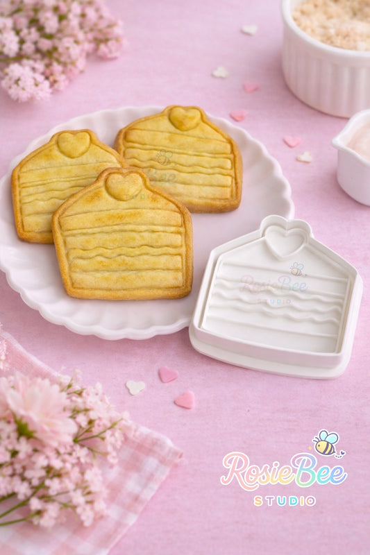 Gebakje koekjesvormpje (cookie cutter) uit de Moji Friends Cosy Café collectie met gebakken gebakjes-koekjes op een wit bordje, pastelroze achtergrond en bloemetjes.